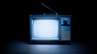 An image - it could be a photograph - a vintage TV sit sat on a surface in the dark, emitting a snowy static glow.