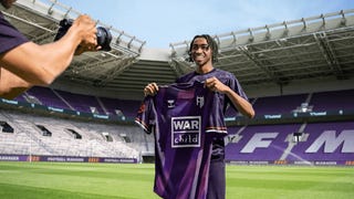 Football Manager key art showing a player holding up a purple kit inside a purple, FM themed stadium for a photograph.