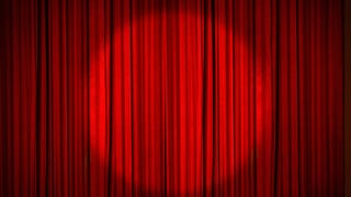 A red stage curtain, drawn, with a circular spotlight shining on the middle of it.