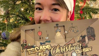 Eurogamer reporter Victoria Kennedy posing half-hidden behind a large cardboard advent calendar. She's wearing a Santa hat and there's a Christmas tree partially visible behind her.